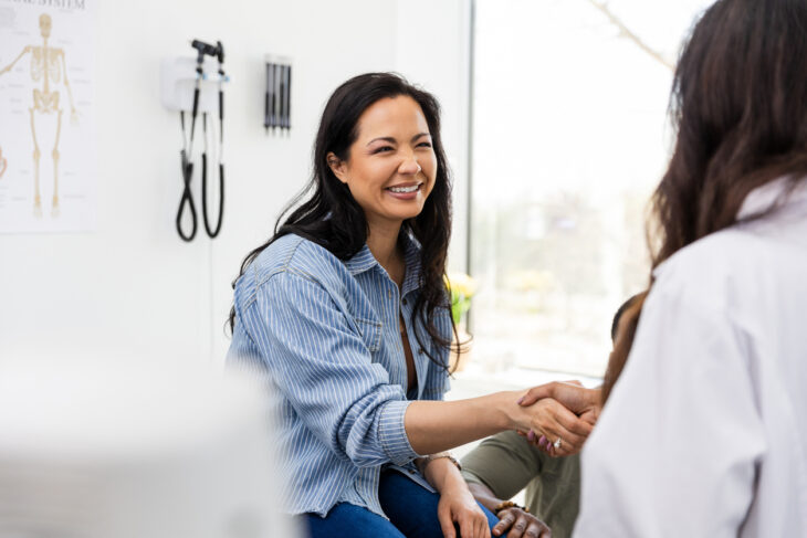 Mid adult female patient smiles and shakes hands with the doctor