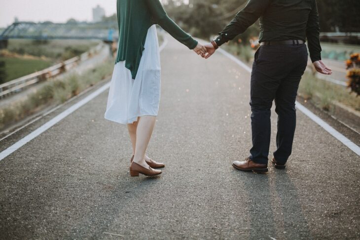 couple holding hand while walking on road