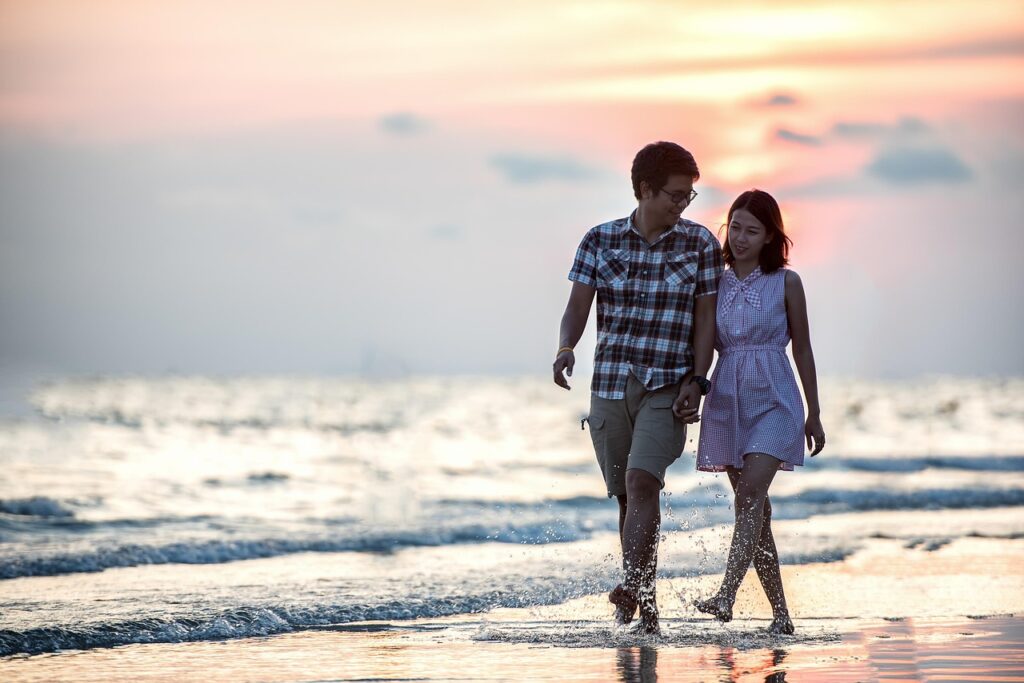 a happy couple walking on beach, holding hands 