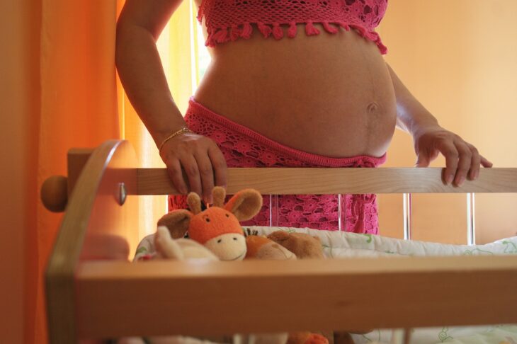 Pregnant woman standing near cradle