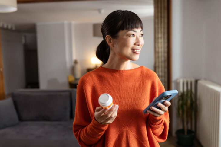 Woman holding a smartphone and a medicine bottle at home