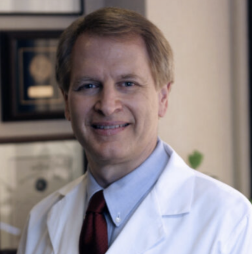Smiling male doctor in a white coat and tie in a medical office setting.
