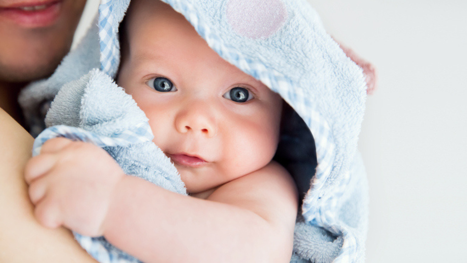 Baby wrapped in a soft blue towel being held by an adult, looking at the camera.
