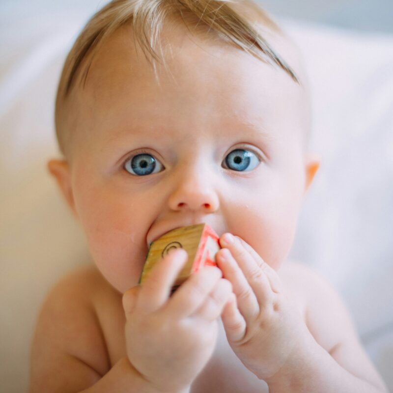 Close-up of a baby with bright blue eyes biting on a small snack pouch held near their mouth.