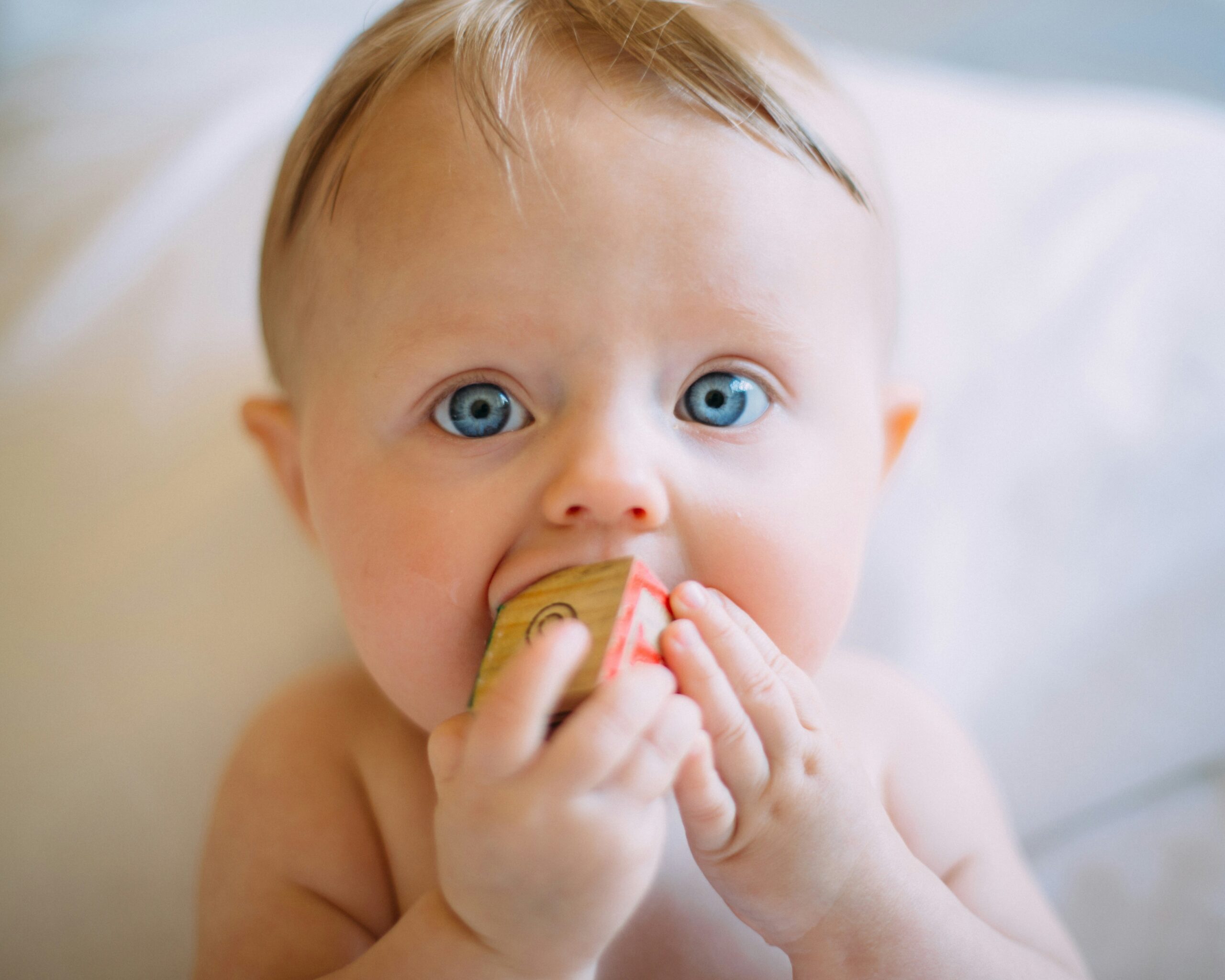 Close-up of a baby with bright blue eyes biting on a small snack pouch held near their mouth.