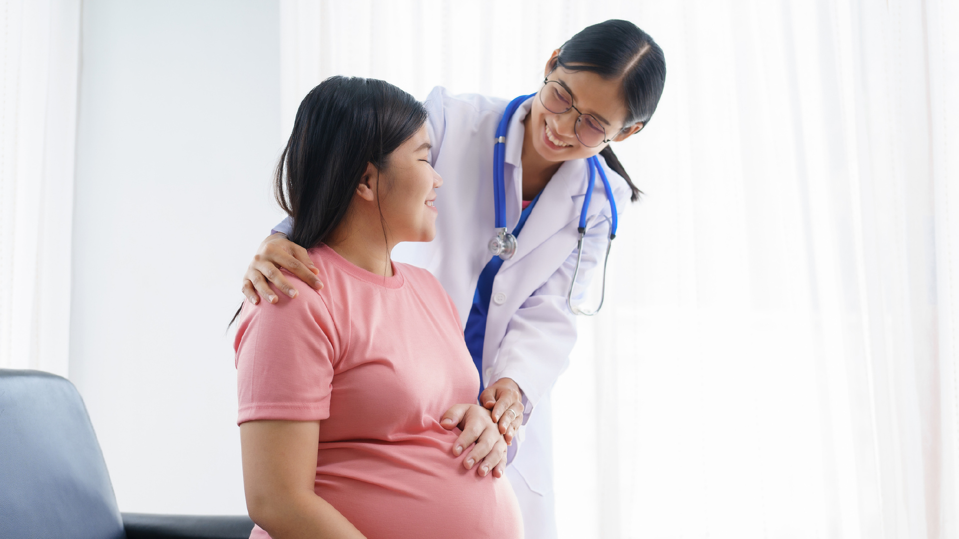 Pregnant woman smiling as a doctor places a hand on her shoulder in a bright clinic.